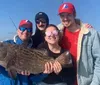 Four people on a boat are smiling with their catch of the day a large fish with a backdrop of clear blue skies and distant city buildings