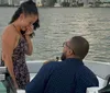 A man is kneeling before a woman appearing to propose to her on a boat with the woman showing an emotional response