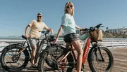 A man and a woman are smiling and posing with their bicycles on a sunny pier, suggesting a leisurely day out.