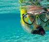 A person is half-submerged in clear blue water wearing snorkeling gear