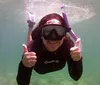 A person in a wetsuit is giving two thumbs-up while snorkeling underwater