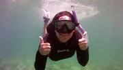 A person in a wetsuit is giving two thumbs-up while snorkeling underwater.