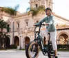 A person is riding a bicycle in front of an ornate building lined with palm trees under a bright sky