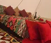 The image shows a cozy bohemian-style glamping setup with a colorful patterned bedspread matching carpet red pillows and romantic touches like a bottle of wine and red roses