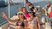 A group of cheerful people are enjoying a sunny day on a boat with drinks, laughing and taking photos.