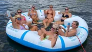 A group of women are relaxing and enjoying drinks on a large inflatable raft on the water.