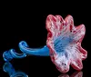 The image shows a beautifully crafted glass sculpture with vibrant blue and red colors resembling a sea creature or flower reflected on a dark surface
