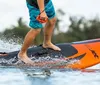 A person is wake surfing on a wave created by a boat on a sunny day with palm trees and houses in the background