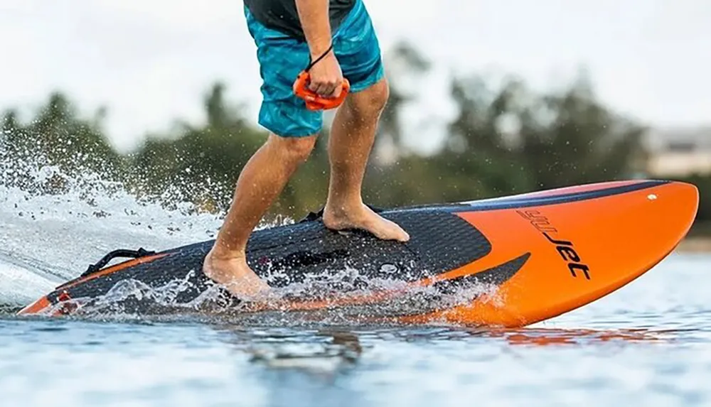 A person is standing on an orange and black paddleboard gliding over water with a splash underfoot