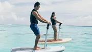 A man and a woman paddleboarding on a calm, clear ocean.