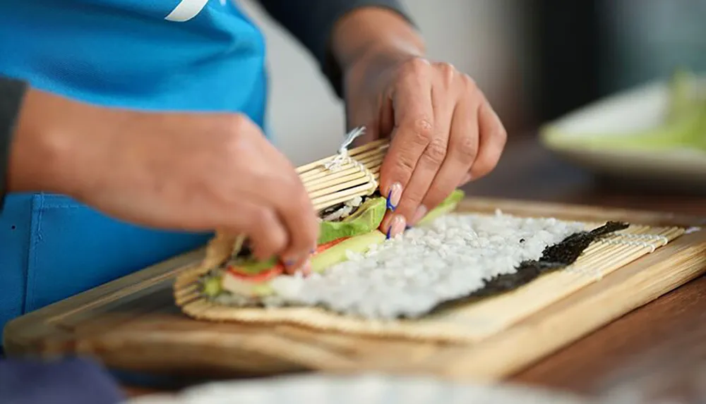 A person is preparing sushi by rolling ingredients in seaweed on a bamboo mat