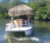 A couple is smiling and embracing near a bamboo bar with a thatch roof on a boat with two other individuals in conversation behind them