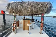 A thatched-roof floating tiki bar with stools and a scenic water backdrop provides a unique and leisurely spot for enjoying drinks on the water.