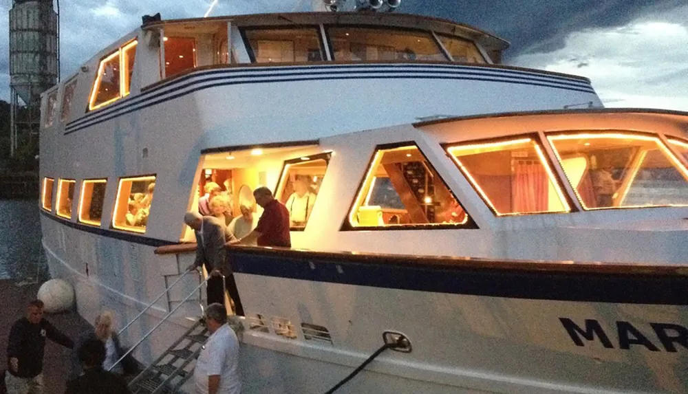 Guests are seen boarding a brightly lit yacht during the evening