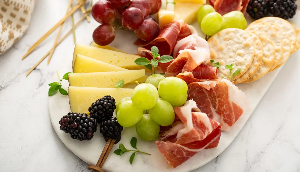 The image showcases a charcuterie board with an assortment of cheeses cured meats crackers and fresh fruits such as grapes and blackberries all arranged for an appetizing display