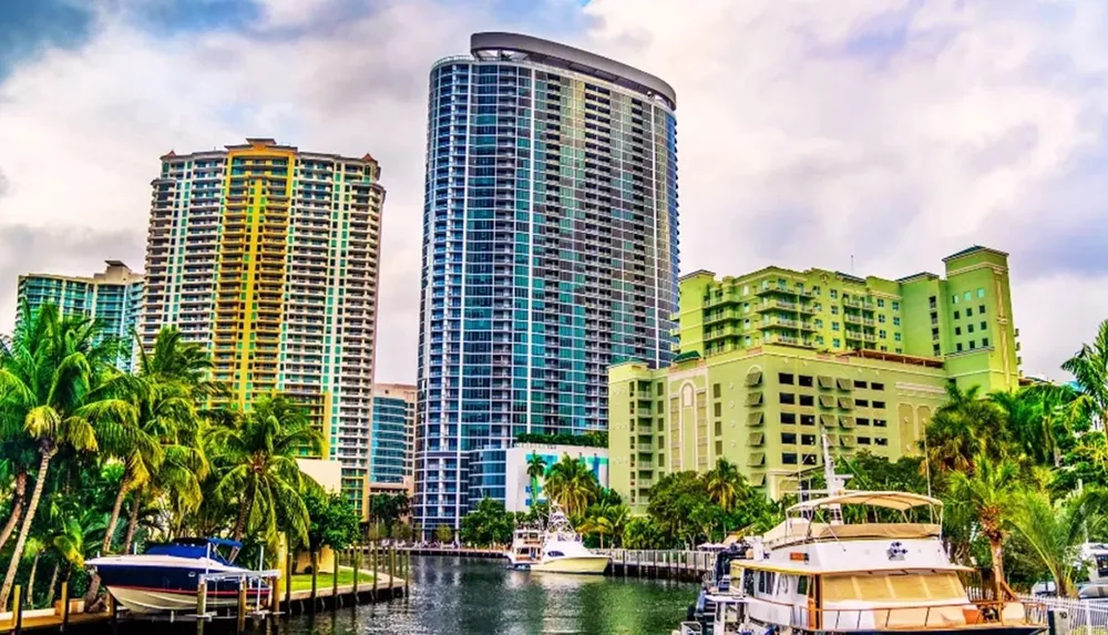 A vibrant waterfront scene with modern high-rise buildings and moored yachts under a cloudy sky