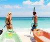 Two people stand by clear kayaks on a sandy beach ready to paddle out into the serene turquoise waters