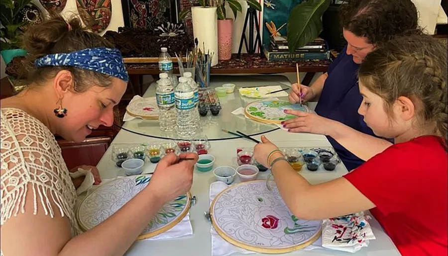 Three people are focused on painting intricate designs on circular canvases during an art session.