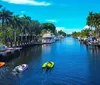 The image shows a tranquil residential canal lined with palm trees and boats docked at private piers under a clear blue sky