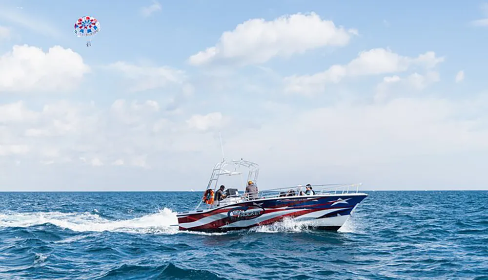 A speedboat is cruising on the water with a parasailer flying in the background under a clear sky