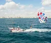 A parasailer is flying above the ocean towed by a speedboat with a coastal city skyline in the background