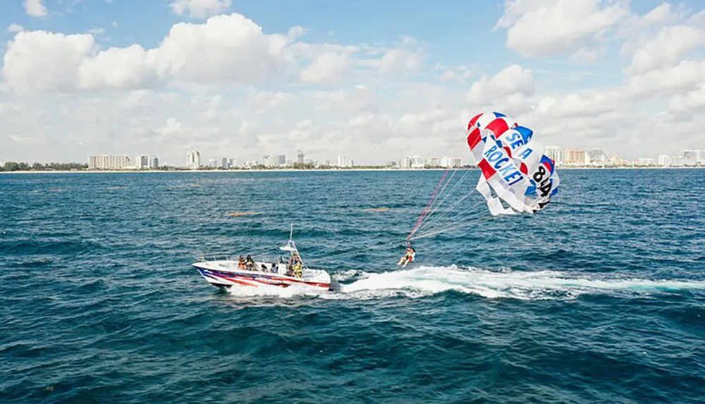 A person is parasailing over the ocean towed by a speeding boat with a coastline visible in the background