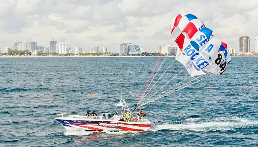 A parasailer is flying above the ocean towed by a speedboat with a coastal city skyline in the background