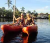 Two people are enjoying kayaking together on a calm waterway lined with palm trees and buildings under a clear sky