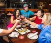 A group of smiling people is toasting at a restaurant table sharing a meal together