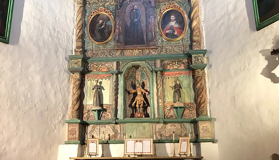 The image shows an ornately decorated Christian altar with religious statues and paintings, set against a white wall.