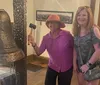 Two smiling women pose beside a large bell one holding a mallet likely to ring the bell