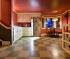 The image shows a colorful kitchen interior with a checkered floor warm lighting and a small dining area visible through an archway