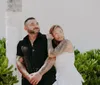 A couple is posing affectionately under a vine-covered pergola in a lush garden setting