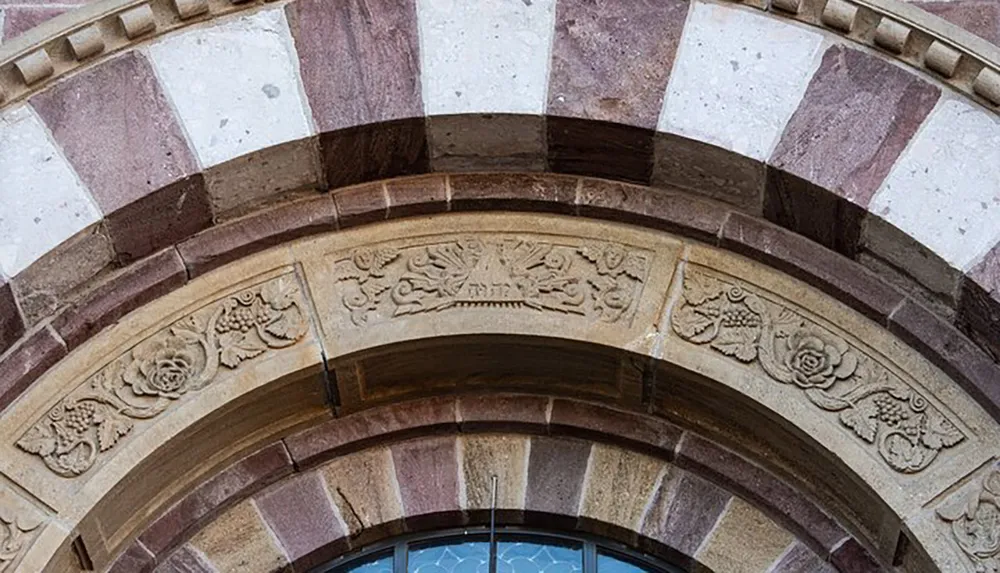 The image displays a close-up of an archway with alternating colored stone and intricate floral carvings above a window