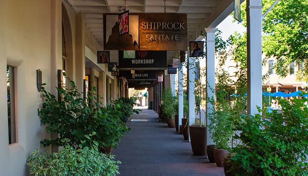 The image shows a shaded outdoor gallery lined with shops and potted plants featuring a sign for Shiprock Santa Fe