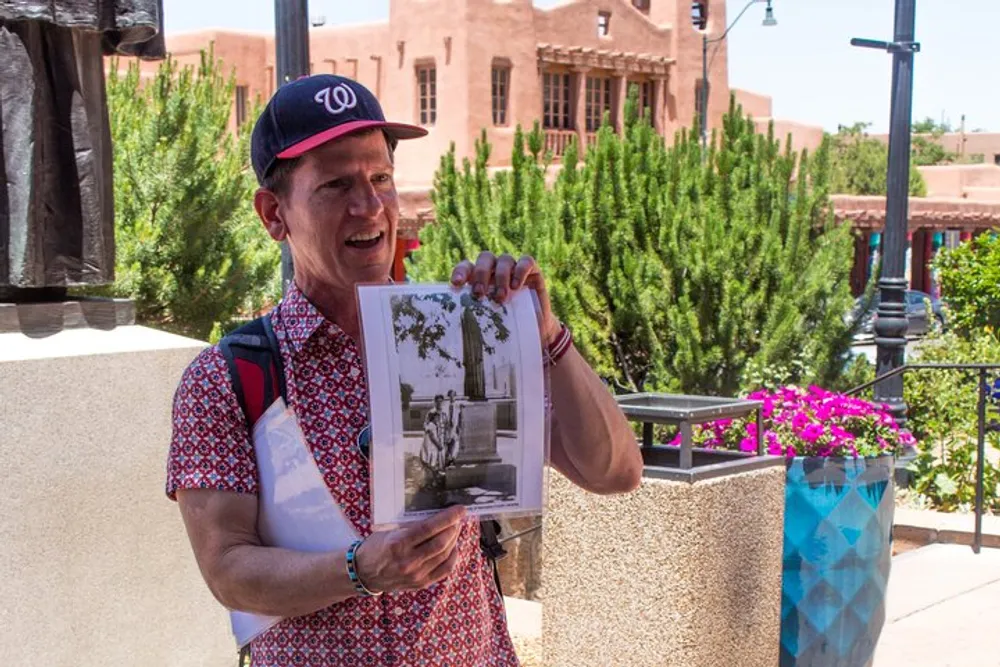 A person is enthusiastically showing a black and white photograph while standing outdoors near plants and a statue