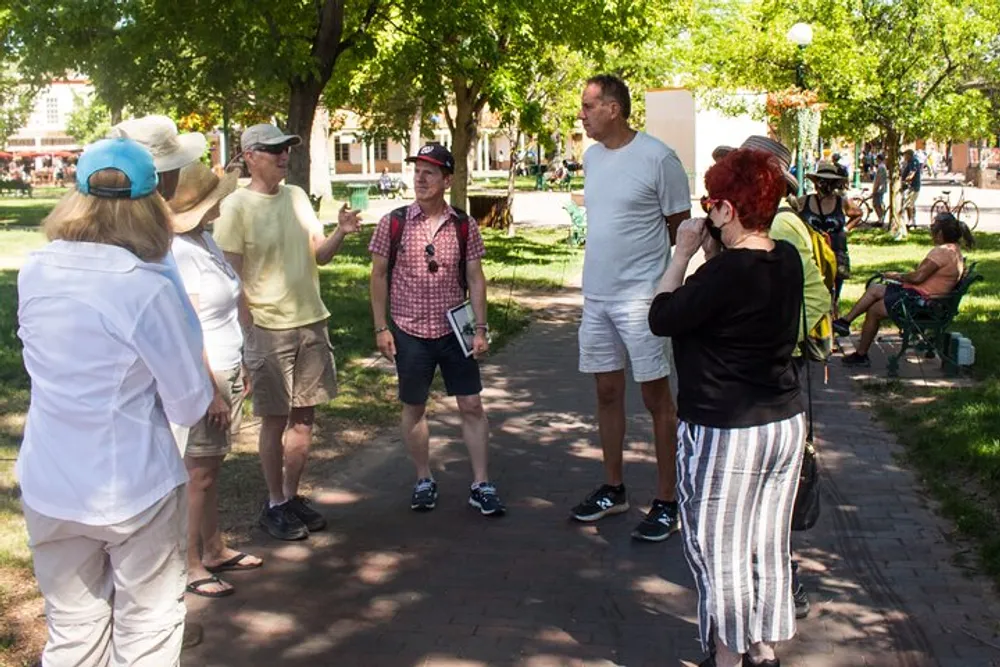 A group of people appear to be engaged in conversation or a guided tour in a sunny park setting