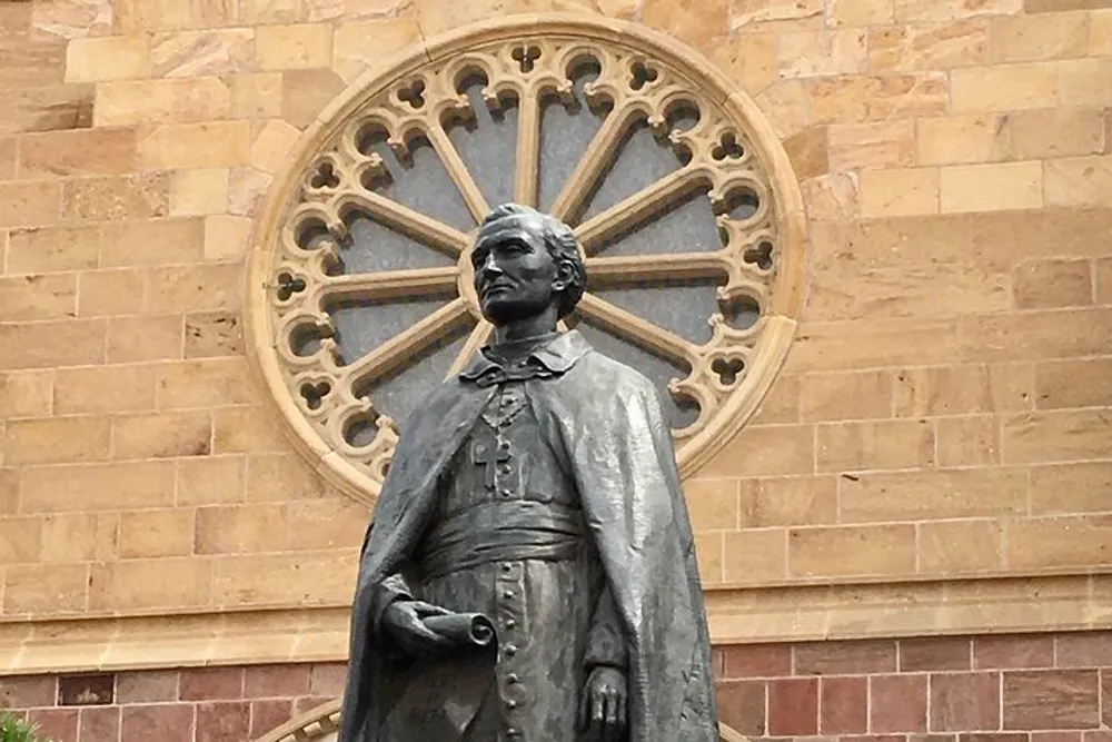 A bronze statue of a robed figure stands in front of a building with an intricate circular window