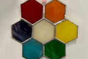 The image shows a collection of hexagonal stained glass panels in various colors assembled together to form a honeycomb-like pattern.