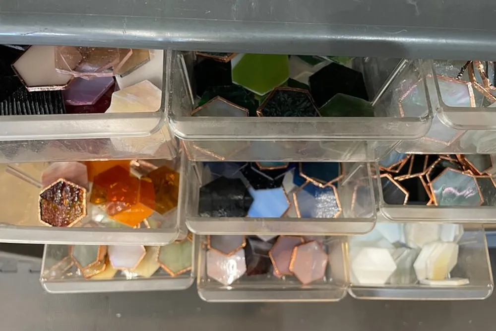 The image shows a plastic organizer with transparent drawers filled with various colorful geometrically shaped objects that resemble gemstones or crystals