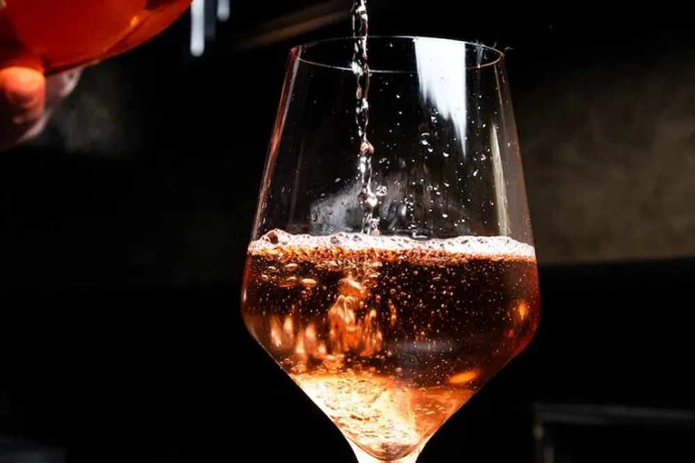 A wine glass is being filled with a sparkling amber liquid against a dark background