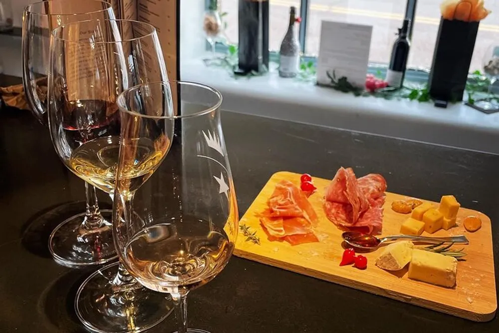 This image shows an elegant arrangement of wine glasses paired with a wooden board hosting an array of cheeses and cured meats possibly suggesting a wine tasting setting