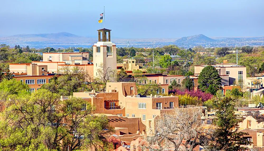 This image shows a southwestern American town with Pueblo-style architecture surrounded by greenery under a clear blue sky