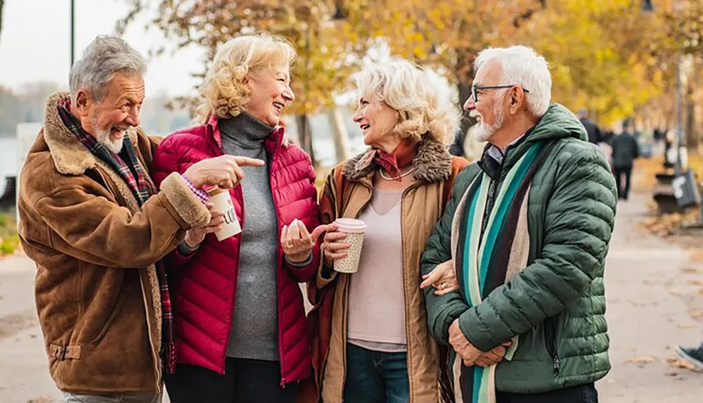 Four older adults are enjoying a lively conversation and laughter together in an autumnal park setting