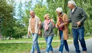 Four senior adults are enjoying a lively conversation while walking together in a green park.