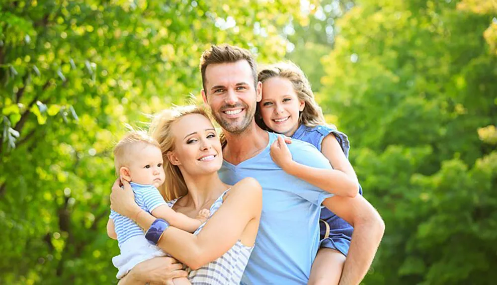 A happy family with two children is smiling outdoors in a natural leafy setting