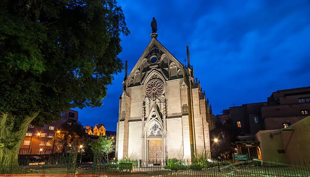 An illuminated Gothic-style mausoleum stands out against a dusk sky in a tranquil urban green space