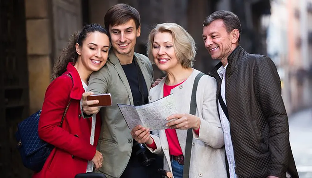 A group of four people likely tourists are smiling and looking at a mobile phone and a map together on a city street