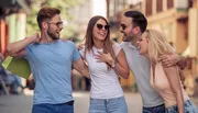 Four friends are laughing and enjoying a lively conversation on a sunny urban street.