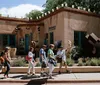 A group of people is walking past an adobe-style building adorned with sculptures under a clear blue sky